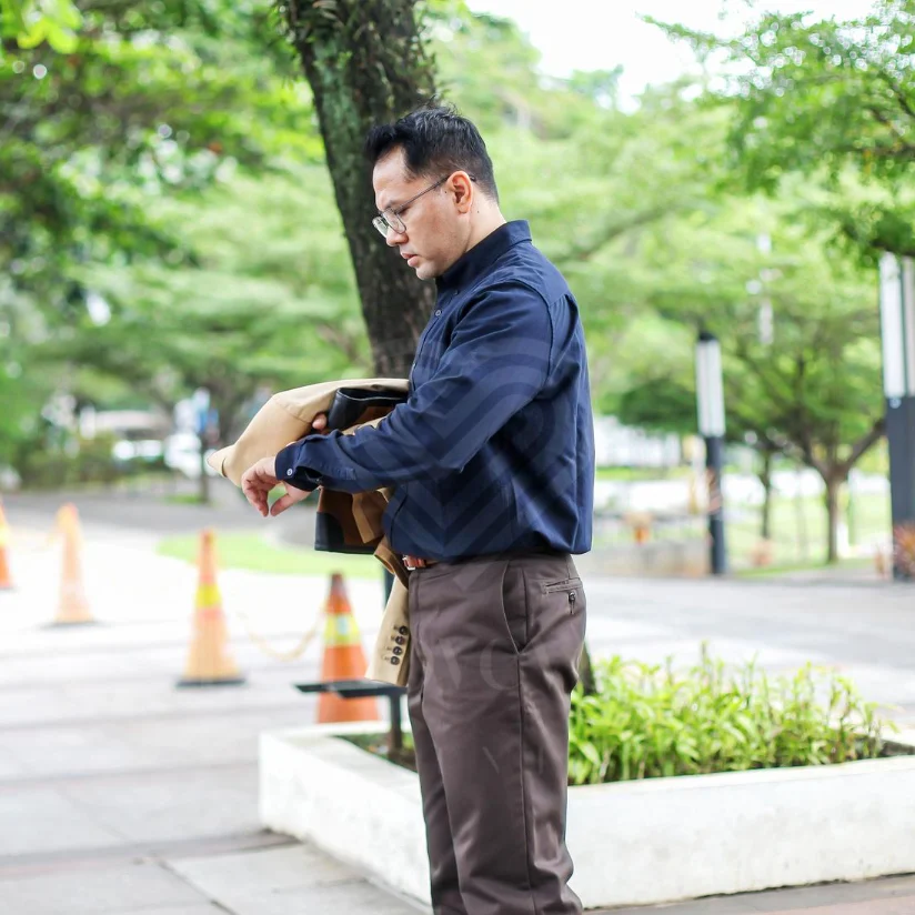 Man checking watch in urban park wearing navy shirt and holding tan jacket