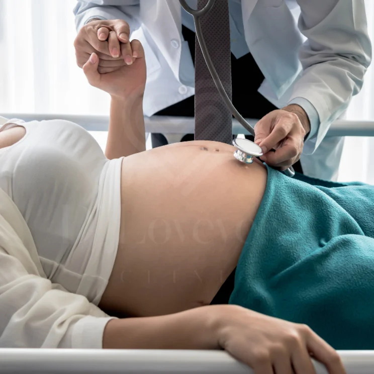 Prenatal checkup: doctor listening to pregnant belly with stethoscope, holding her hand