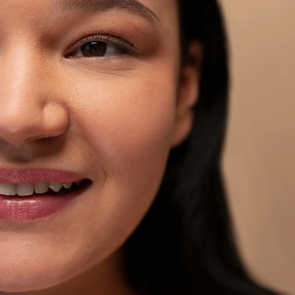 Warm close-up portrait of a smiling woman showing left half of face, brown eye visible