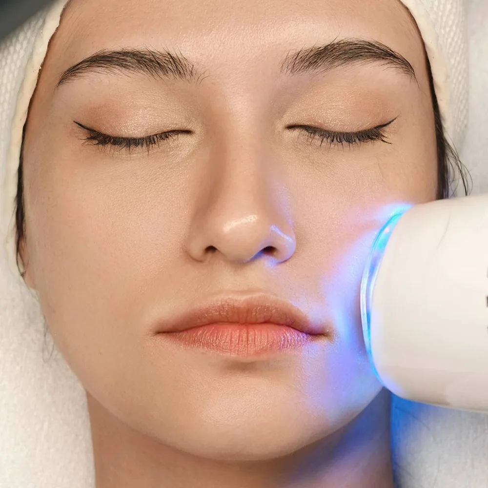 D Aura Plus LED facial treatment: blue light device on cheek for radiant skin