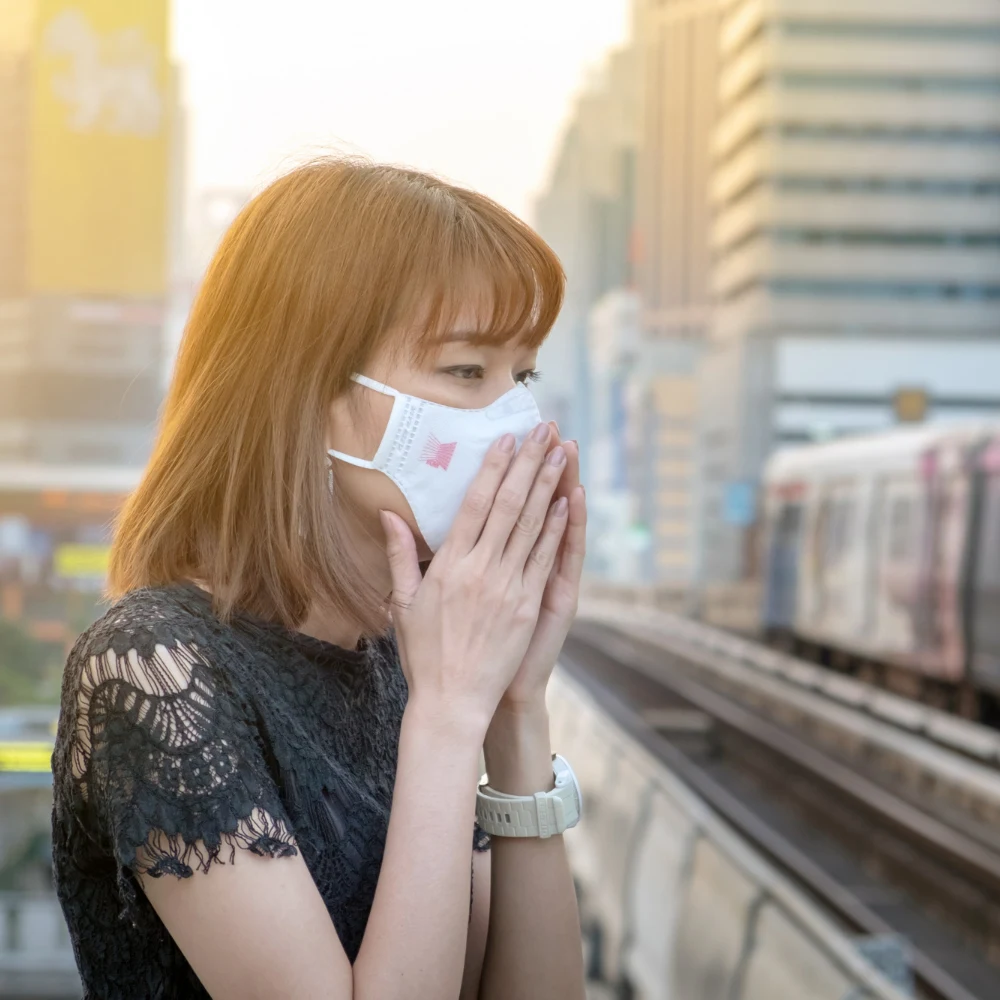 Masked commuter shields face from PM2.5 pollution beside elevated train in sunlit city