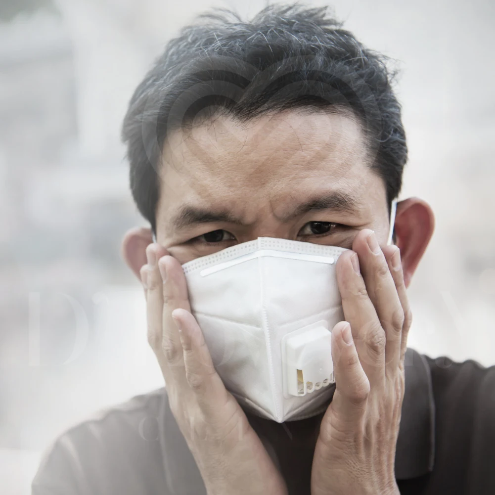 Close-up of person pressing PM2.5 respirator mask to face, furrowed brow.
