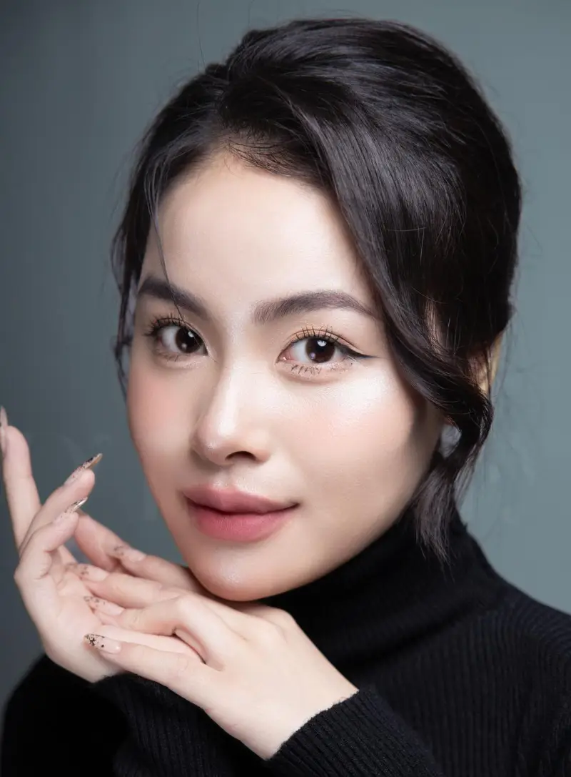Editorial close-up portrait of woman with dolly-eye winged eyeliner, black turtleneck, chin on hands