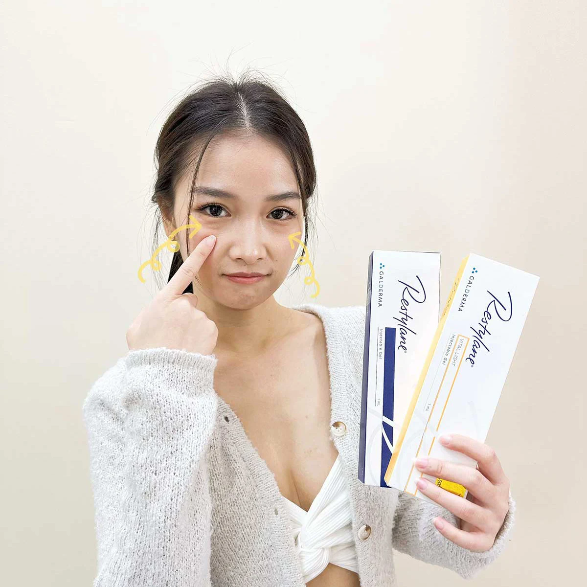 Woman points to under-eye bags holding dermal filler boxes