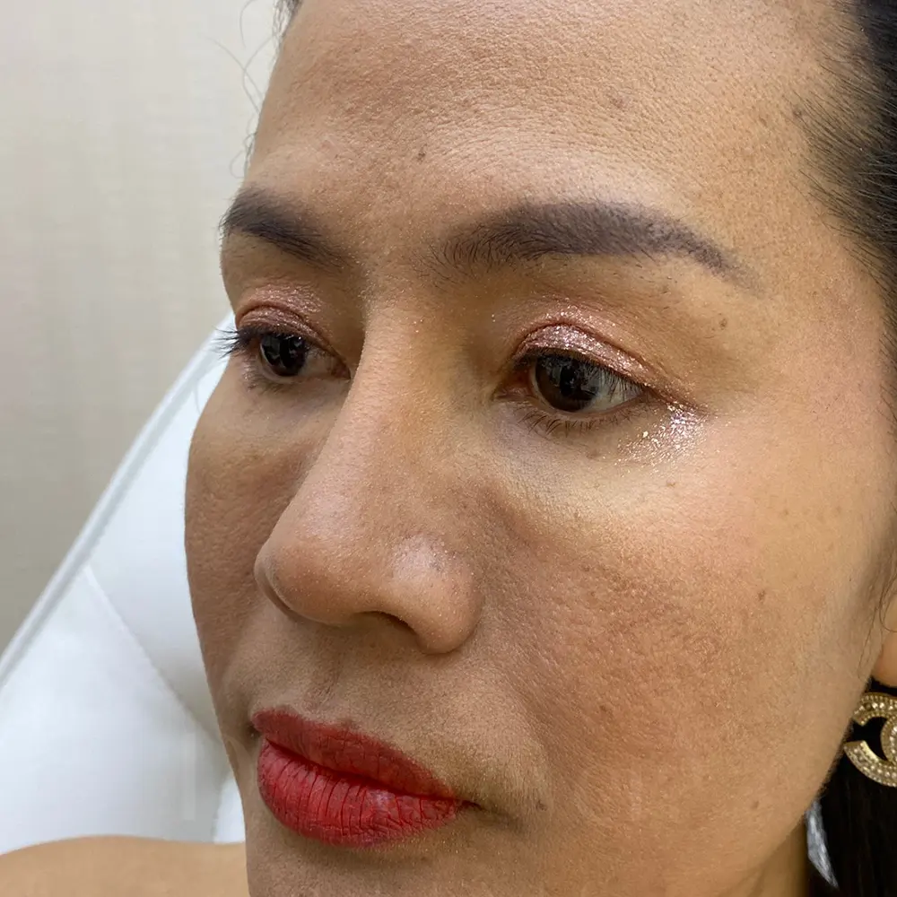 Close-up woman with rose-gold eyeshadow, matte red lips, visible under-eye texture, gold earring.