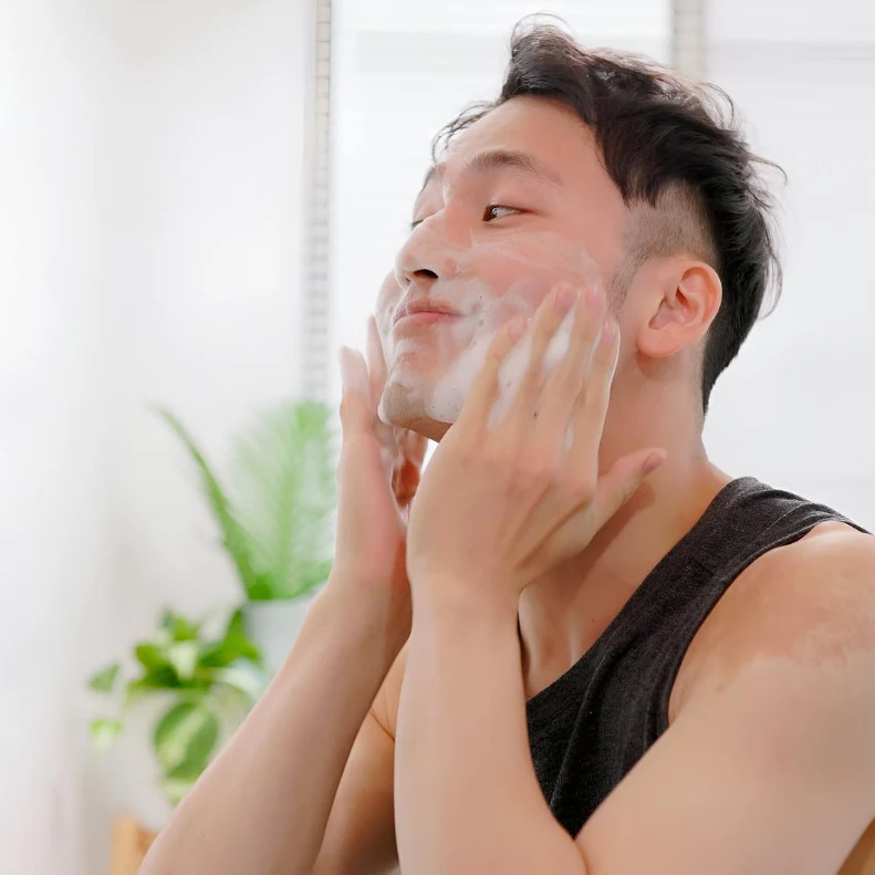 Person washing face with thick foam cleanser in at-home skincare routine