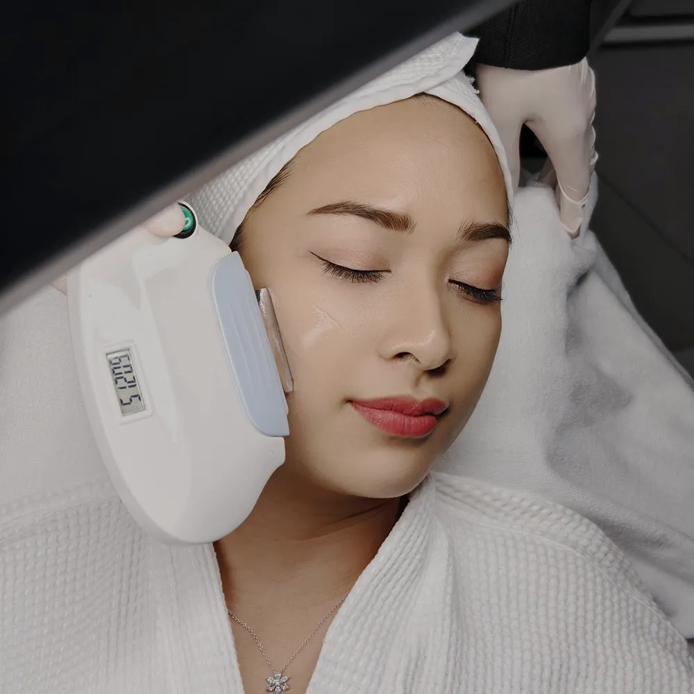 Woman receiving noninvasive laser facial (IPL/Pico) with handheld device in spa clinic.