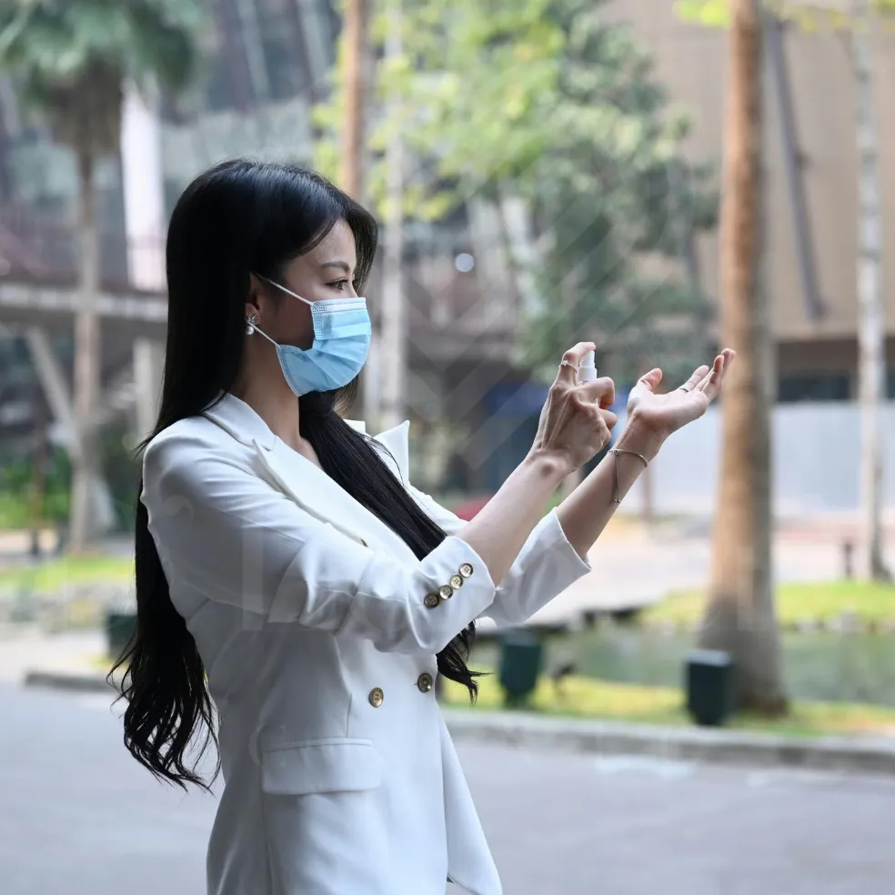 Professional woman in blazer and mask applying hand sanitizer in urban plaza
